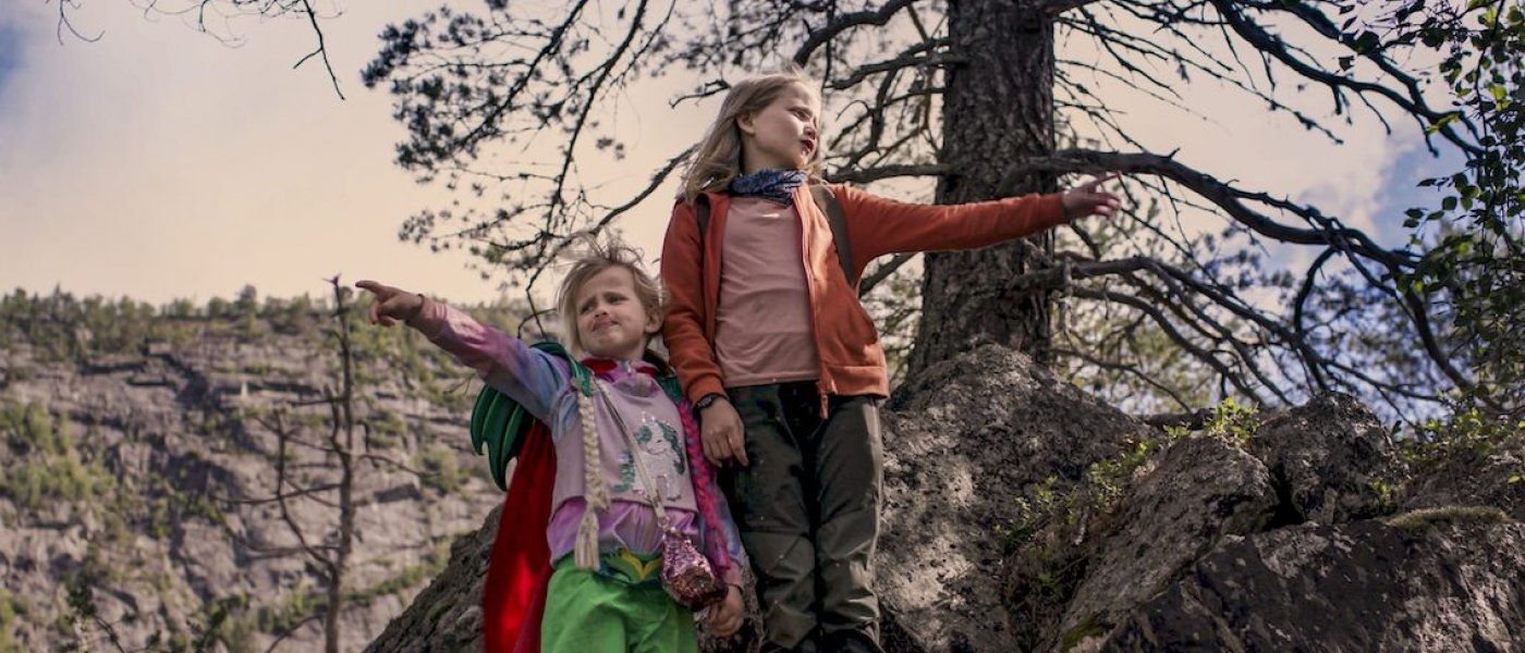 Två flickor står på ett berg och pekar i olika riktningar.